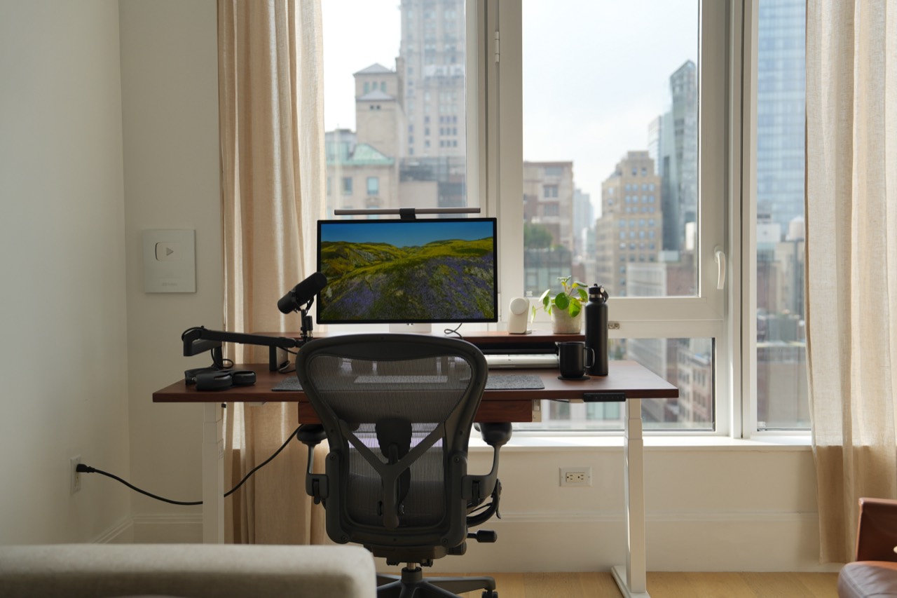 Front view of the walnut desk, Studio Display, and Aeron chair against the NYC skyline
